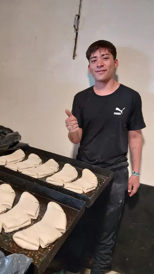 Un integrante del equipo, con el pulgar en alto, junto a dos bandejas con los panes ya formados
