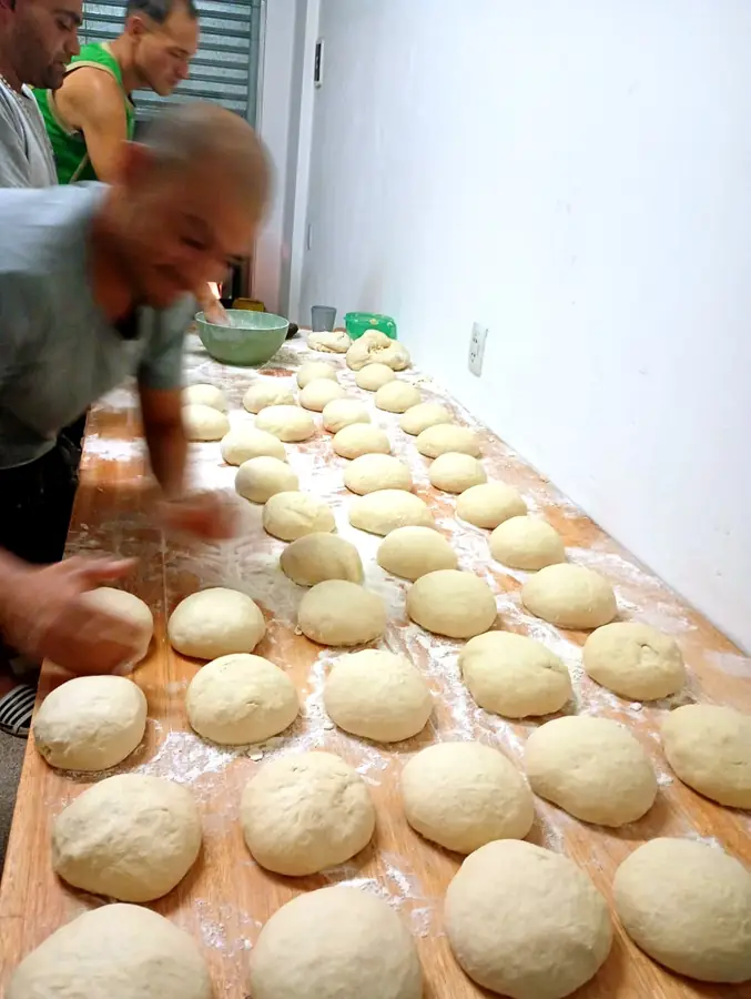 Sobre la mesada enharinada, decenas de bollos de masa alineados en filas mientras el equipo sigue armando