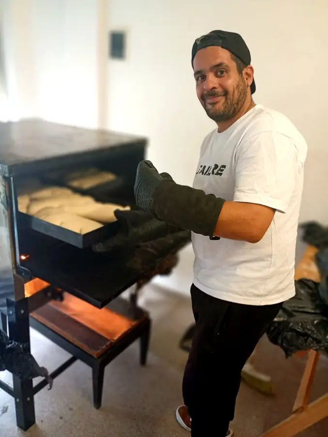 Un integrante del equipo, con guantes de horno, saca una bandeja de panes del horno encendido